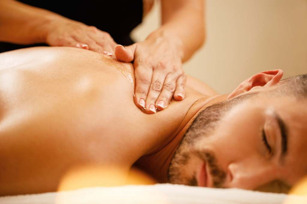 massage therapist performing back massage on male client