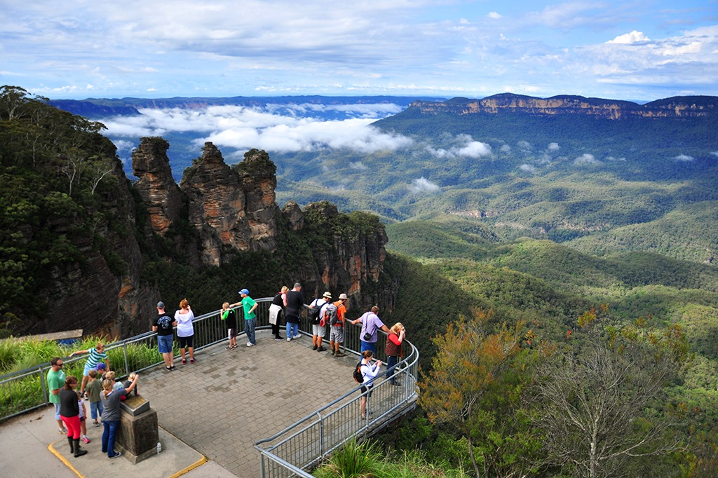 View of the Three Sisters rock formation in the Blue Mountains with visitors at a lookout overlooking forest valleys and scenic landscapes