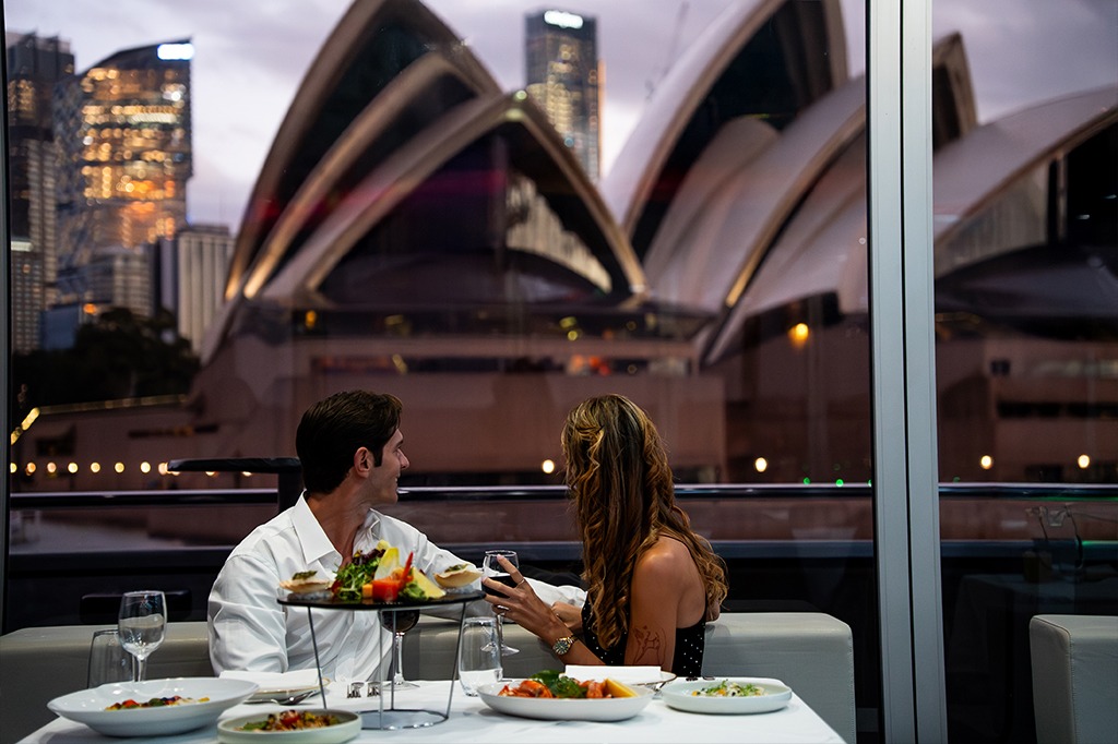 Couple enjoying dinner on a Sydney Harbour dinner cruise with the Sydney Opera House in the background at night