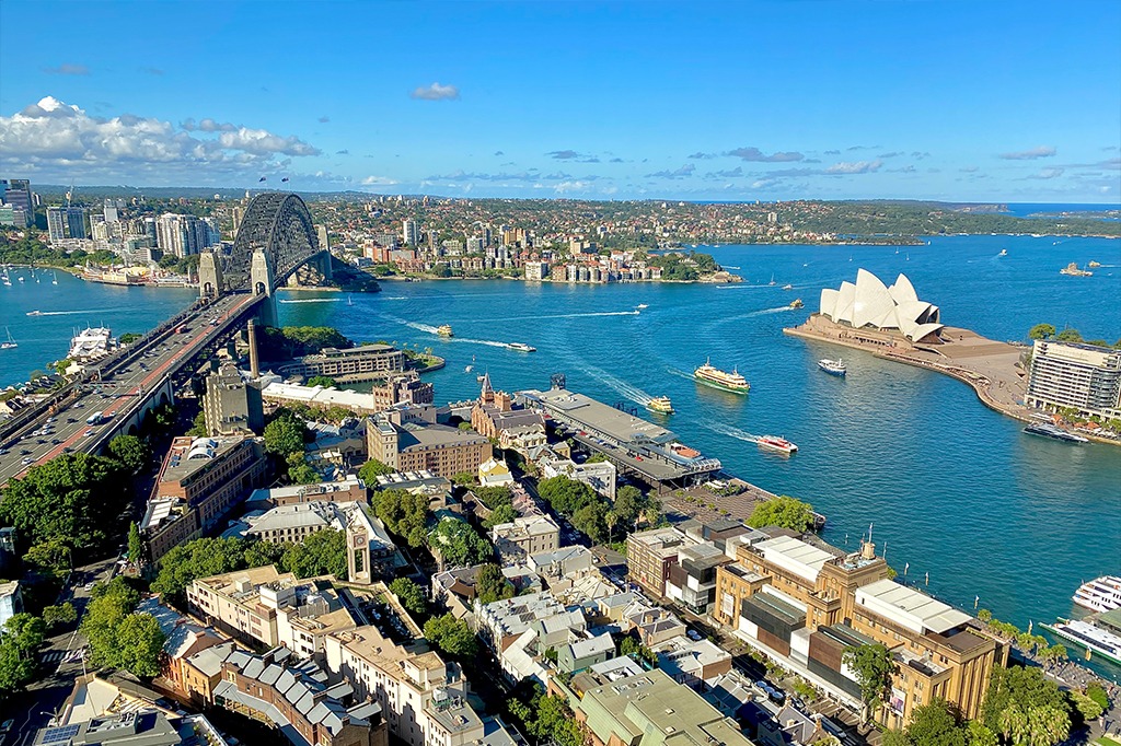 Aerial view of Sydney Harbour featuring the Sydney Harbour Bridge, Sydney Opera House, boats on the water and the city skyline under a clear blue sky
