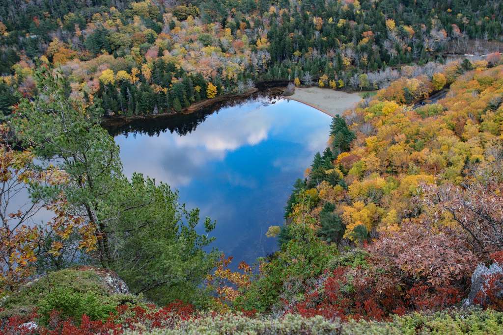Echo Lake reflecting the sky, ringed by yellow, orange, and red fall foliage, seen from a cliff above