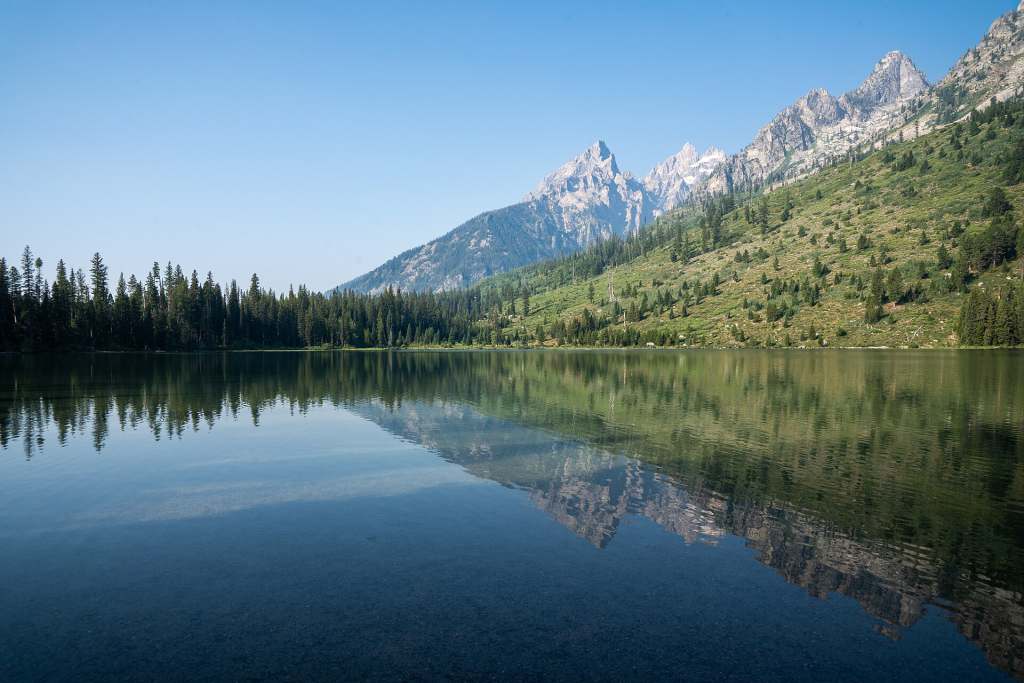 Calm String Lake reflecting the Teton peaks and the forested slopes above the shore