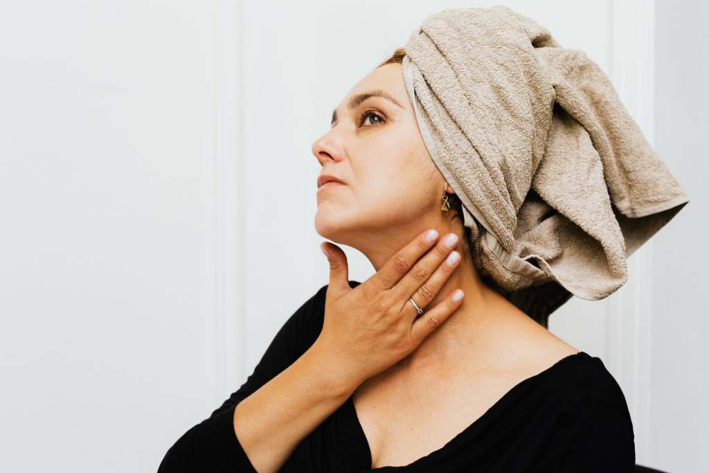 Traveler in her 50s applying balm to her hands beside an airplane window, skin care for travel after 40